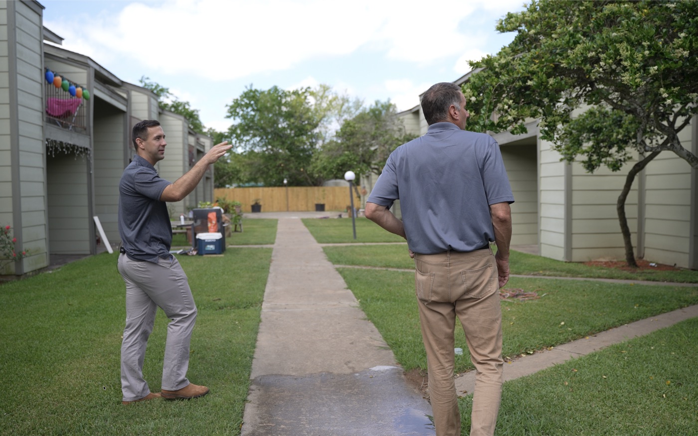 Two men walking the grounds of an apartment property, one pointing out work on the building.